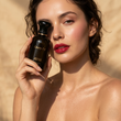 Woman holding a black perfume bottle labeled 'Cherry Pop' by ZUVA against a beige background